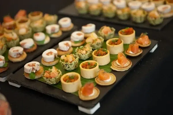 Trays of Thai canapés ready for a drinks reception: papaya salad boats, mini spring rolls, satay and crispy bites with edible flowers.
