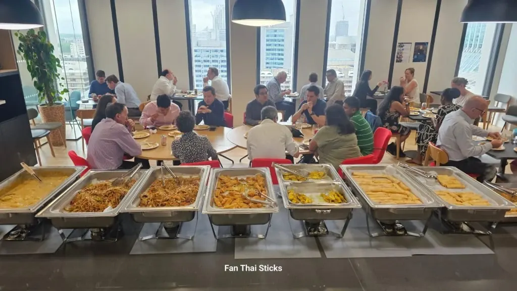 Staff eating an office lunch with Thai dishes in the foreground